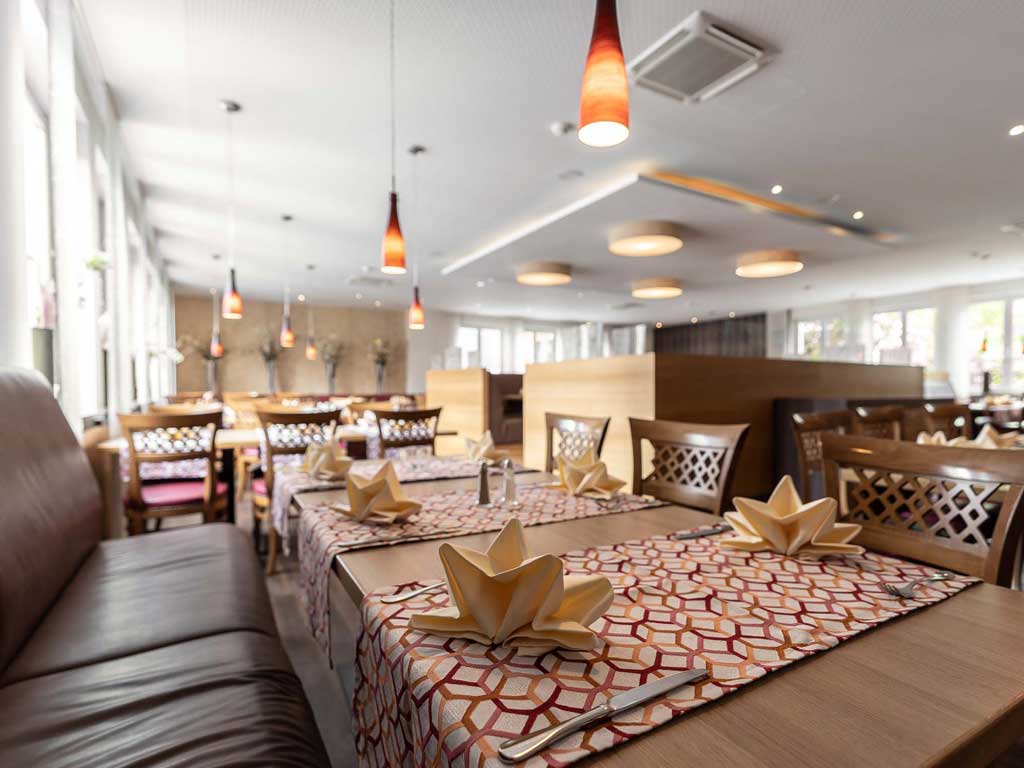 Das große Restaurant im Altmühltal hat viele Tische mit Stühlen und Sitzbänken, sowie hägende Lampen und große Fenster