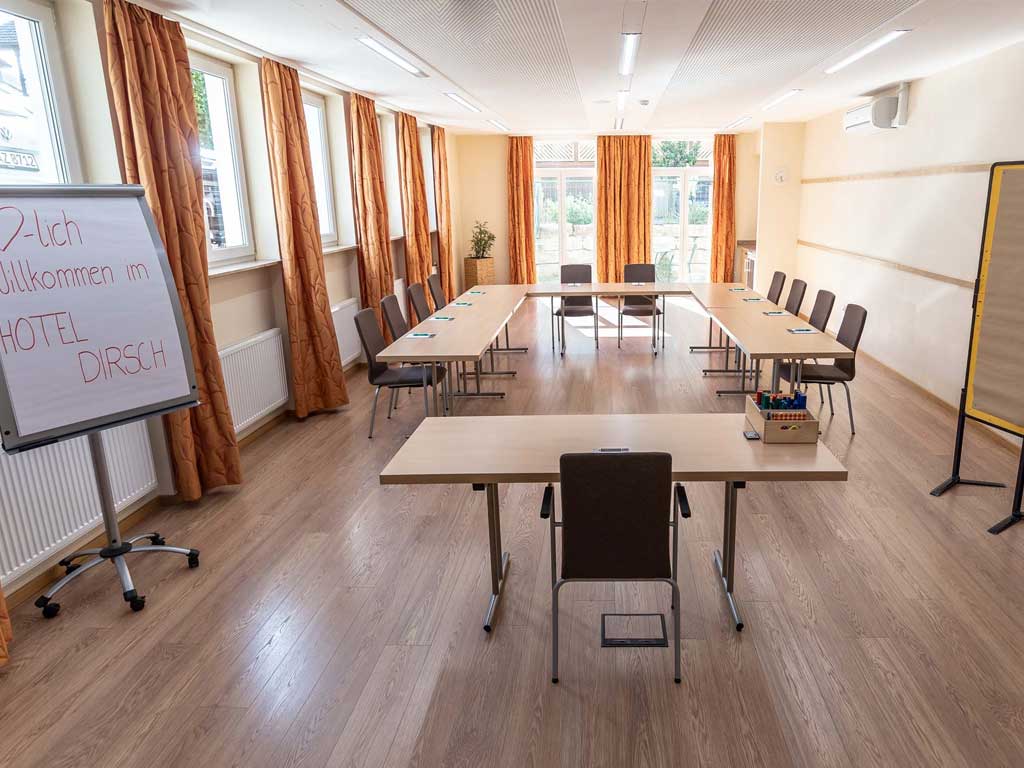 Im Tagungszimmer des Tagungshotels im Altmühltal gibt es große Tische und viele Stühle, sowie ein Whiteboard mit dem Schriftzug 