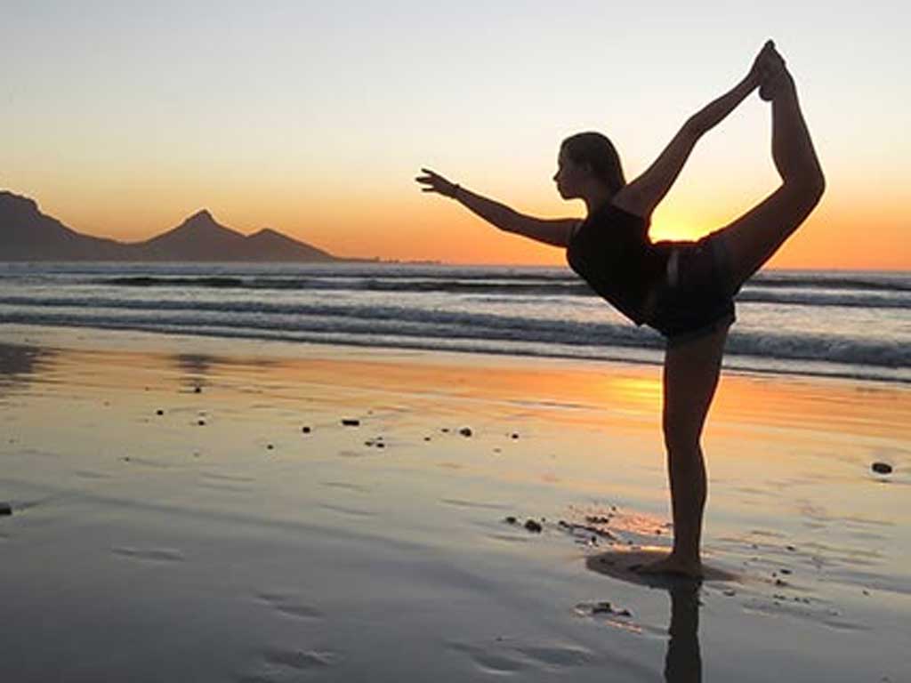 Eine Frau macht am Strand während des Sonnenuntergangs Yoga