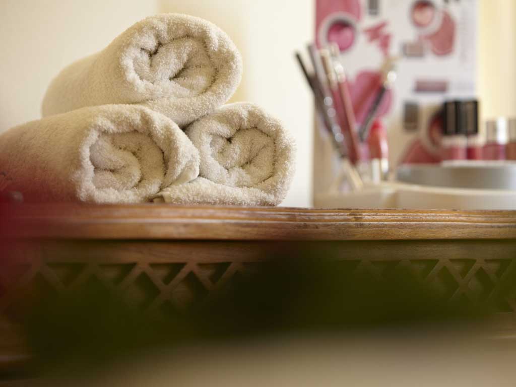 Drei weiße Handücher liegen eingerollt mit Pinseln und Nagellacken auf einem Holztisch im Wellnessraum für Schönheitsbehandlungen