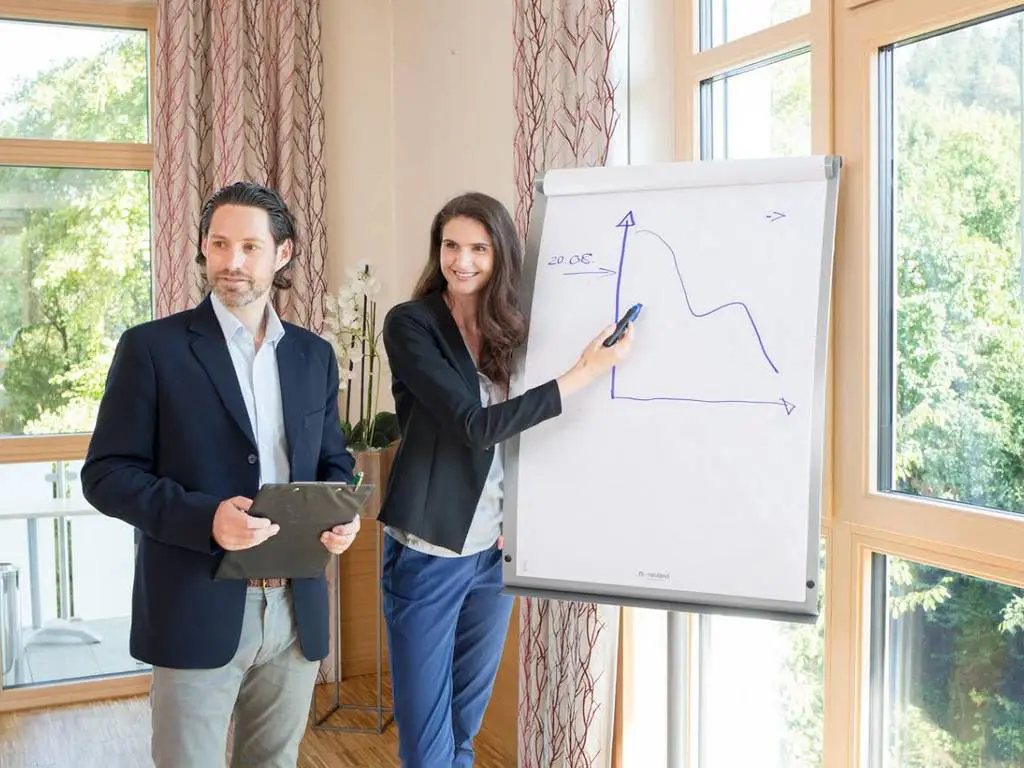 Ein Mann und eine Frau erklären einen Graphen auf einem Flipchart im Tagungshotel im Altlmühltal